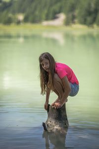 Portrait of girl crouching on tree stump in lake