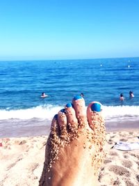 Low section of woman on beach against blue sky