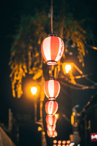 Close-up of illuminated lamp hanging on street light at night