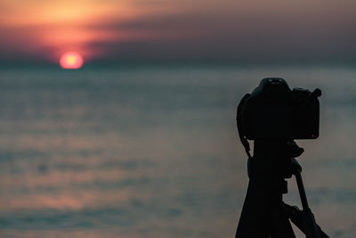 Close-up of coin-operated binoculars against sea during sunset