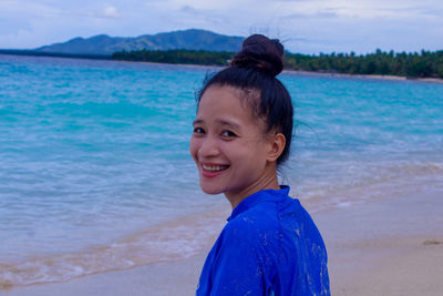 Portrait of young woman standing at beach against sky