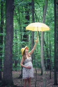Full length of woman standing by tree trunk in forest
