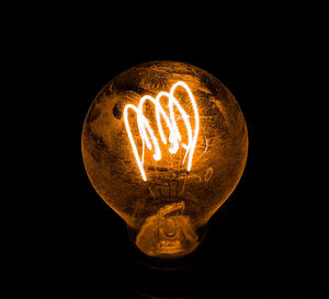 Close-up of illuminated light bulb against black background