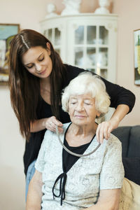 Granddaughter putting on necklace to grandmother at home