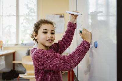 Portrait of smiling girl writing on whiteboard in classroom