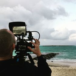 Rear view of man photographing at beach against sky