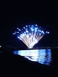 Firework display over sea against sky at night