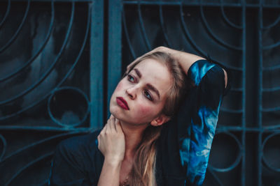 Beautiful woman looking away while standing against metal gate