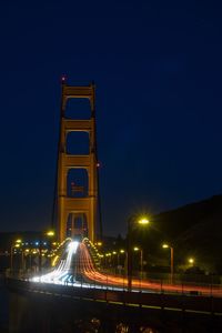 Light trails on road against clear blue sky at night