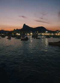 Illuminated boats on sea at harbor during sunset