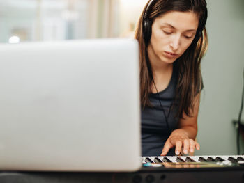 Smiling woman wearing headphones playing piano at home