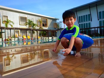 Full length of cute boy crouching with inflatable ring by swimming pool