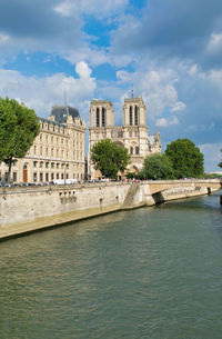 Buildings by river against cloudy sky