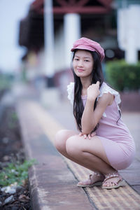 Portrait of young woman crouching on footpath