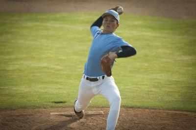 Pitcher in light blue and white jersey during wind up on a baseball field.