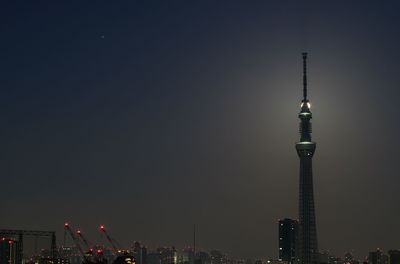 Communications tower in city against sky at night