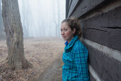 Portrait of woman standing by wall on field during foggy weather