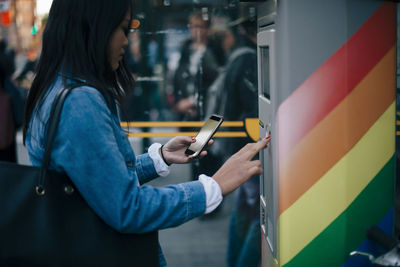 Side view of teenage girl using smart phone and atm machine