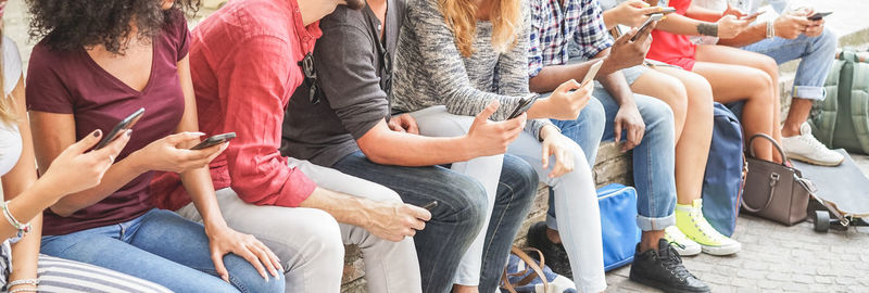 Panoramic view people using phone while sitting on retaining wall