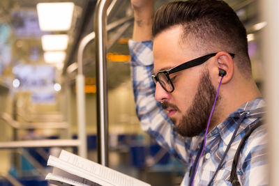 Close-up of young man with headphone reading book while traveling in train