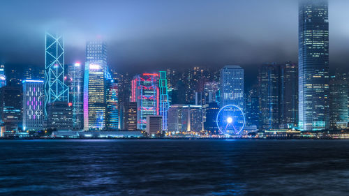 Illuminated city by sea against sky at night