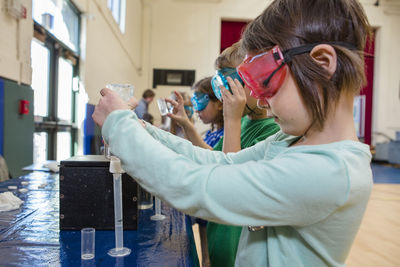 A little girl in safety goggles measures liquid into a test tube