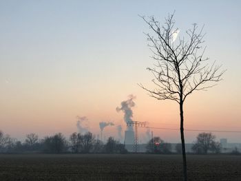 Smoke emitting from factory against sky at sunset