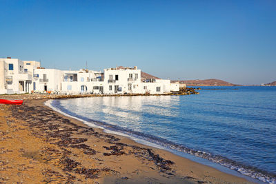 Buildings by sea against clear blue sky