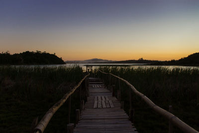 Walkway by lake during sunset