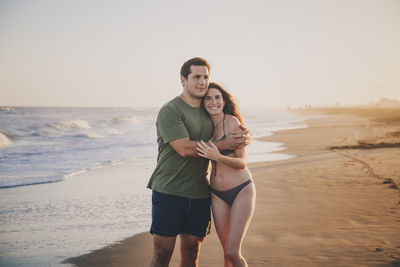 Portrait of a couple standing at beach during sunset