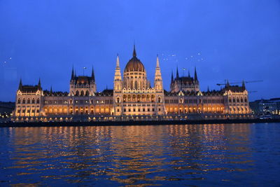 Hungarian parliament building by river against clear blue sky