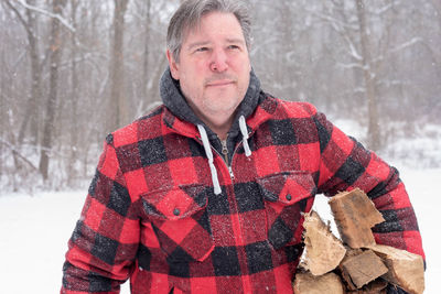 Midsection of mature man with wood during snowfall