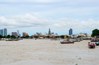 Boats on chao phraya river against cloudy sky