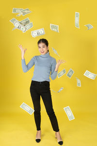 Portrait of smiling young woman standing against yellow background