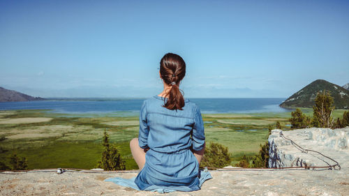 Rear view of woman sitting by sea against clear sky