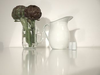 Artichokes in jug with jar on glass table at home