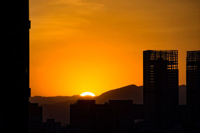 Silhouette city against orange sky during sunset