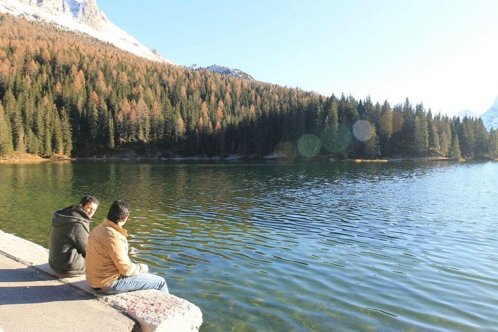 water, leisure activity, lifestyles, lake, tranquility, clear sky, tree, scenics, mountain, tranquil scene, men, nature, beauty in nature, sitting, rock - object, person, relaxation, sunlight