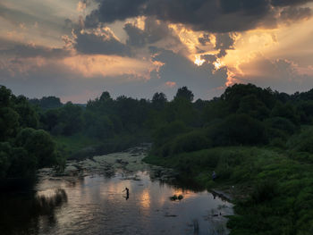 Scenic view of trees growing by dubna river against cloudy sky during sunset