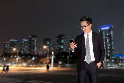 Businessman with hand in pocket using smart phone in city at night