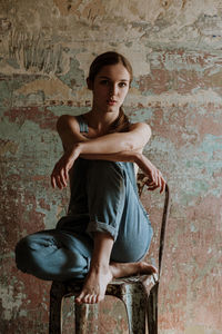 Portrait of a young woman sitting against wall