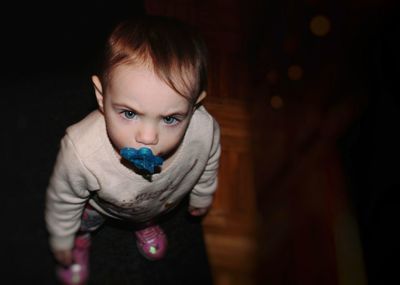 Portrait of cute girl sucking pacifier in darkroom