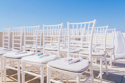 Empty chairs and tables at beach against clear blue sky