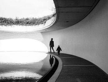 Rear view of father and son walking on footpath by pond