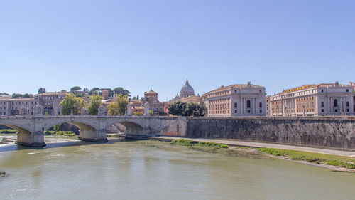 Arch bridge over river with st peter basilica in background against clear sky