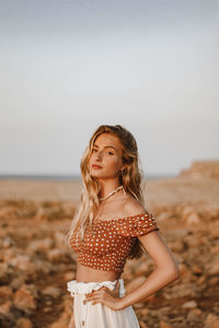 Portrait of beautiful woman standing at beach against sky