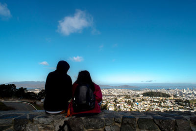 Rear view of people looking at cityscape against blue sky