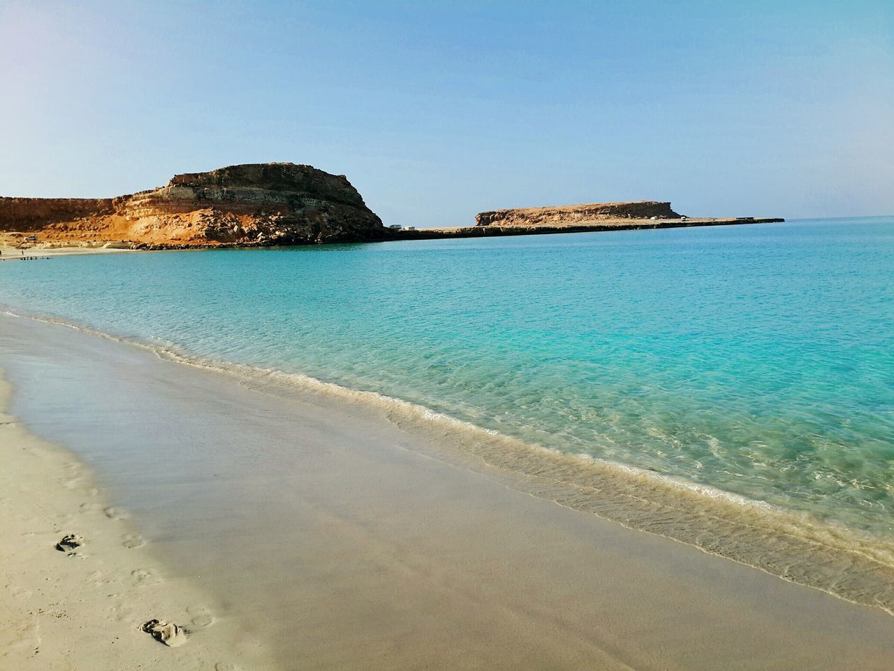 sea, water, beach, sand, clear sky, horizon over water, shore, scenics, tranquil scene, tranquility, blue, beauty in nature, nature, coastline, rock formation, idyllic, incidental people, copy space, vacations, cliff