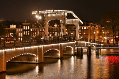 Illuminated bridge over river in city at night