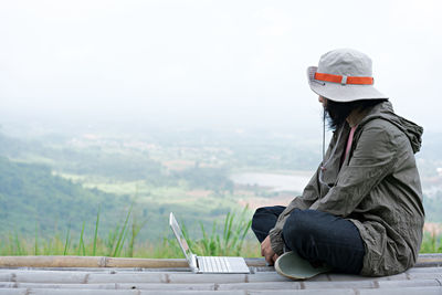 Man sitting on mountain against sky